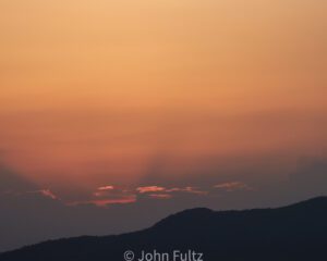 A sunset with the sun setting over mountains.