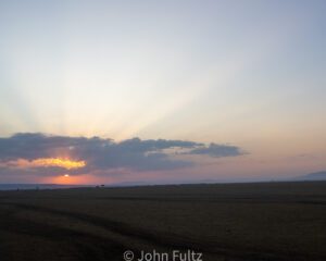 A sunset over an open field with the sun setting.